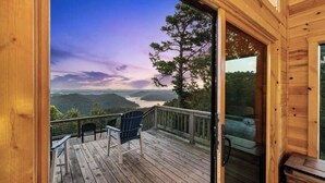 Terraza de madera con sillas y una vista panorámica de un río y montañas.