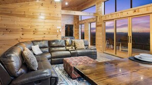 Una sala de estar acogedora con un sofá de cuero, una mesa de centro de madera y un gran ventanal corredero que da a un balcón con vistas panorámicas.