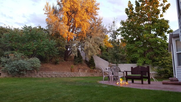 A backyard with a fire pit, a wooden bench, and a metal chair.