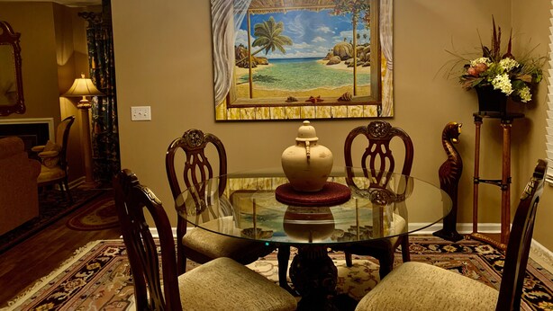 Un coin repas avec une table en verre, des chaises en bois, un vase décoratif et un tableau représentant une scène de plage.