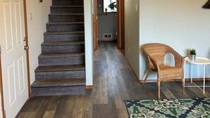 A staircase leading to a second floor, a wicker chair, a small table with a plant, and a patterned rug.