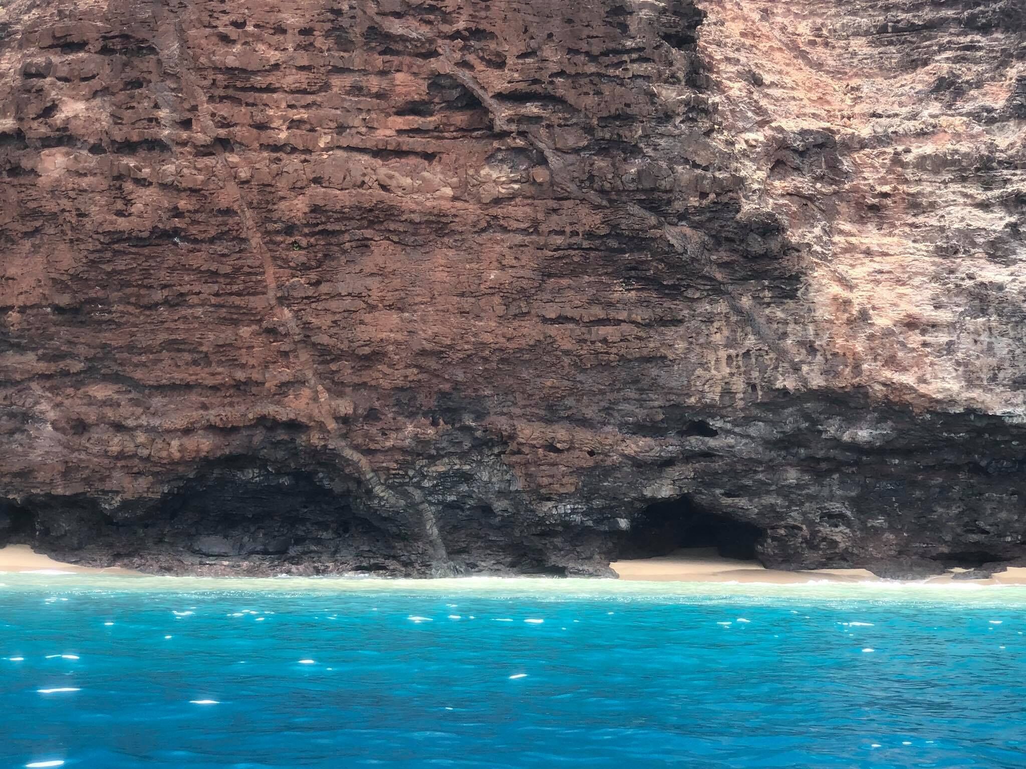 Eine felsige Klippe mit Strand und klarem, blauem Wasser.