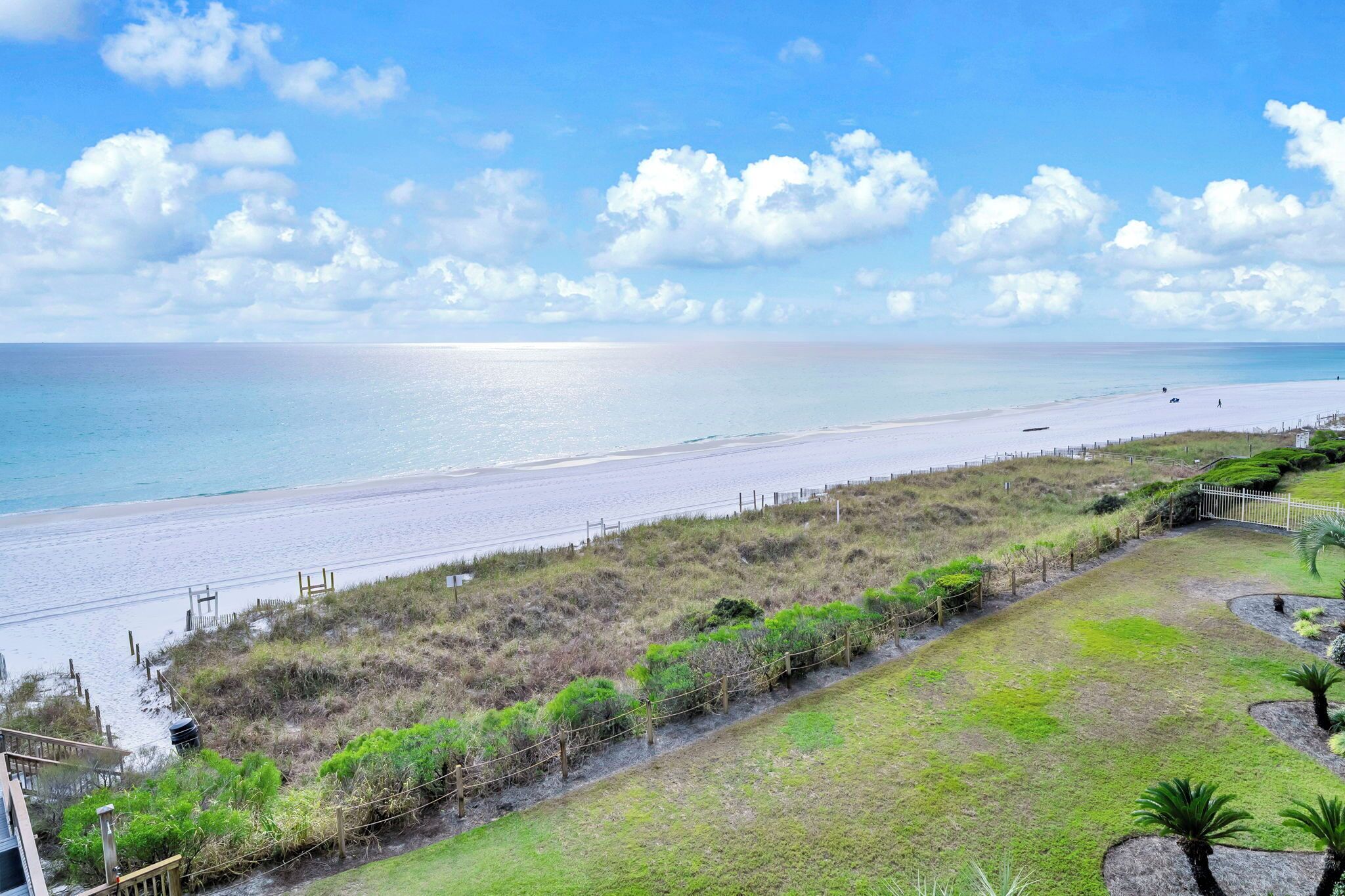 A coastal view with a beach, grassy areas, and a fence.