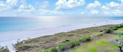 A coastal view with a beach, grassy areas, and a fence.