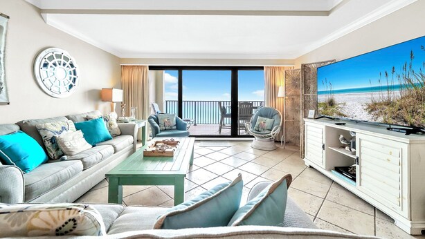 Un salon spacieux doté d’un grand téléviseur, d’un ensemble de canapés, d’une table basse et offrant une vue sur la plage grâce aux portes-fenêtres donnant sur le balcon.