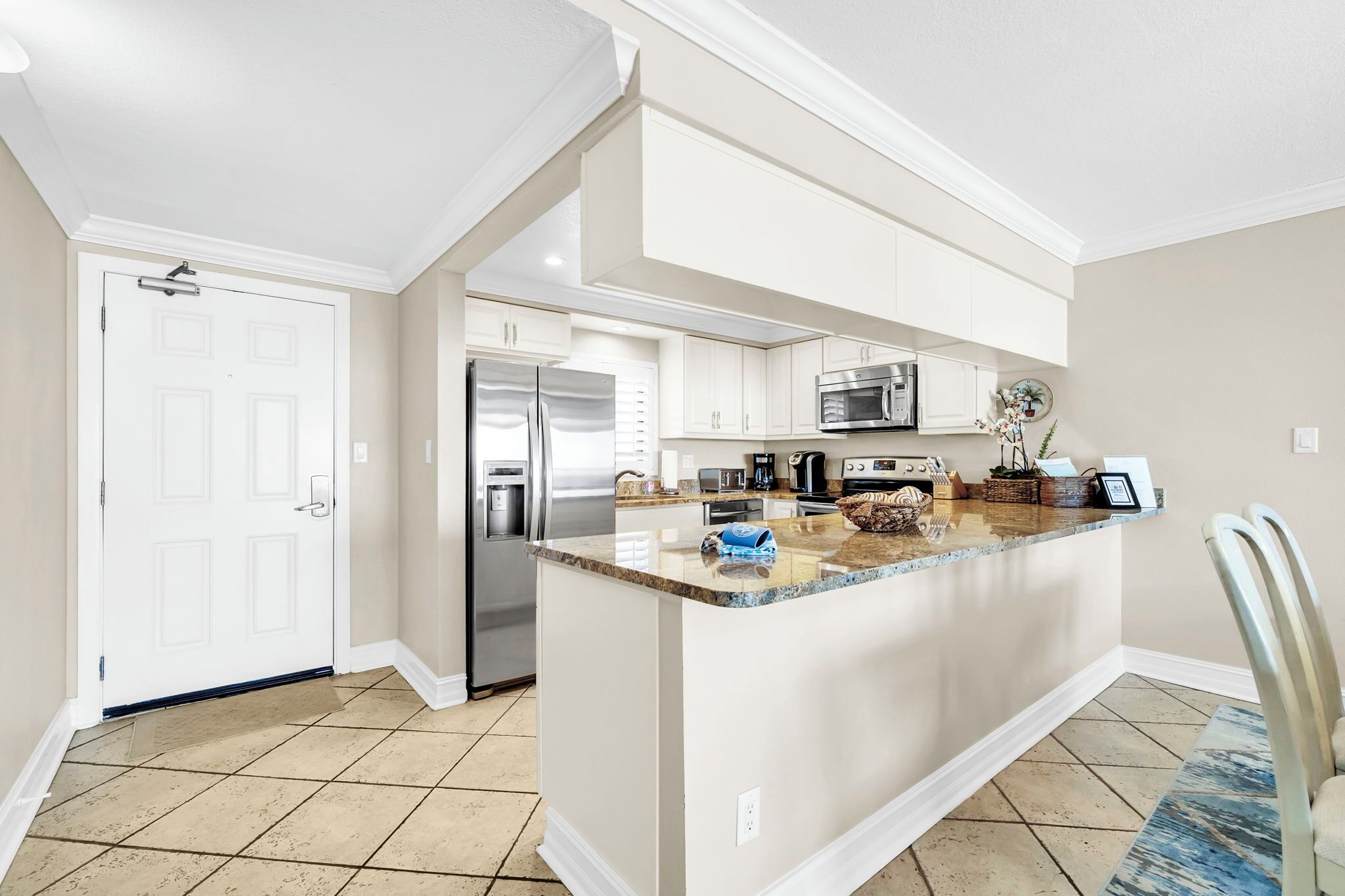 Una cocina con isla central, muebles blancos, electrodomésticos de acero inoxidable y suelo de baldosas.