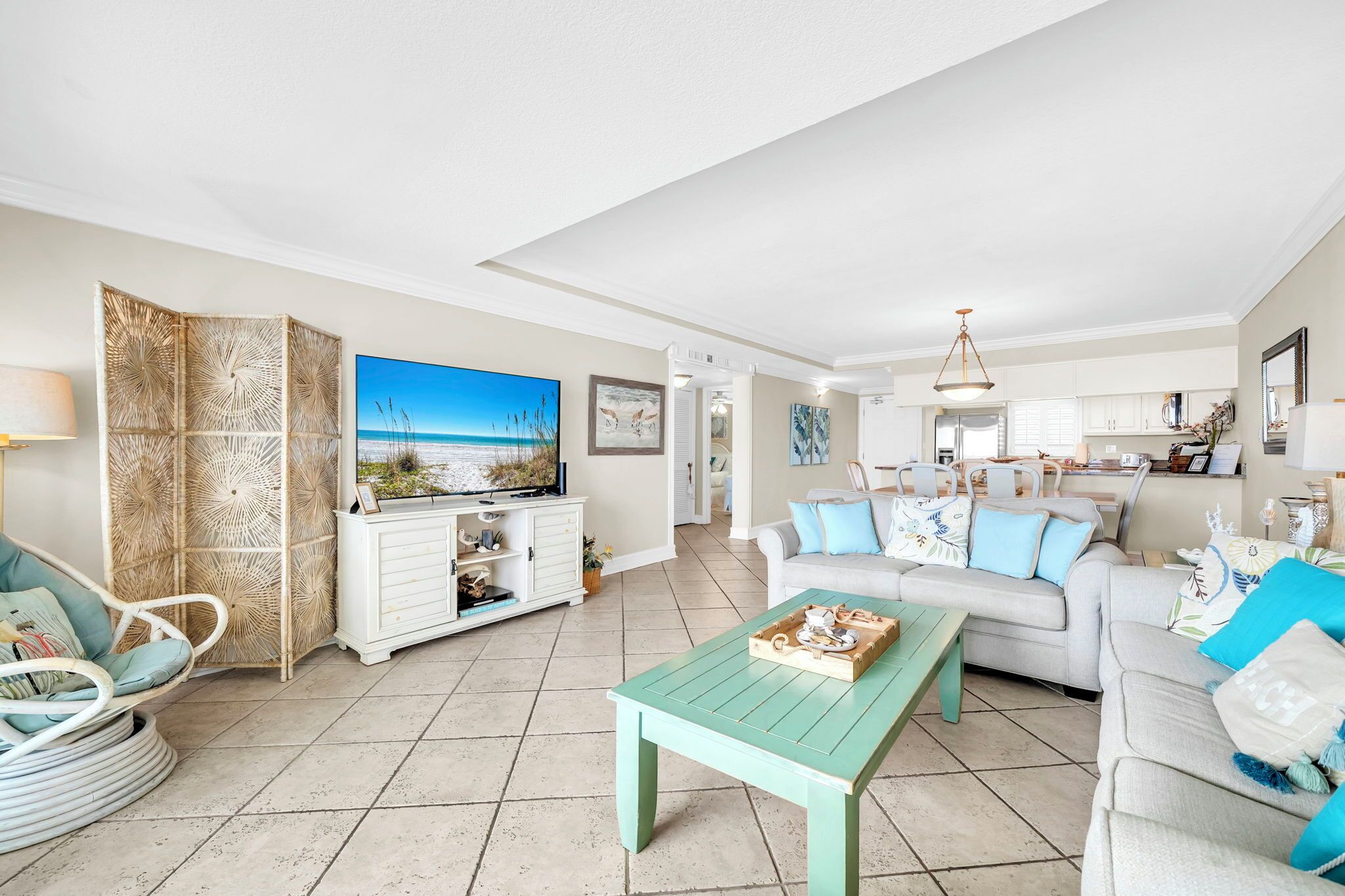 A spacious living room with a large TV, a dining table, and a sofa with blue cushions.