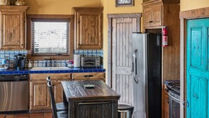 A kitchen with wooden cabinets, a tiled backsplash, a stainless steel refrigerator, and a teal door. - SkyHouse cabin on the West Rim (Canyon)