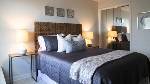 A modern bedroom with a large bed, two bedside tables with lamps, a woven headboard, and a mirror on the wall.