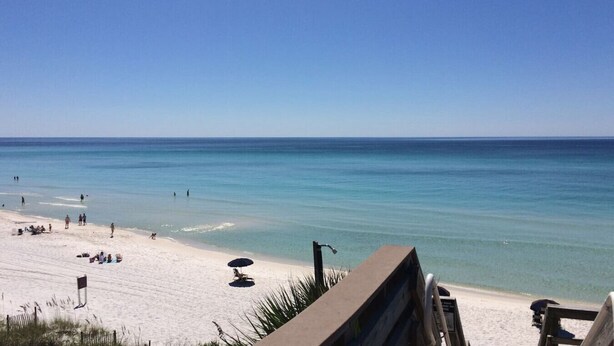 A beach with clear blue water, sandy shore, and a few people.