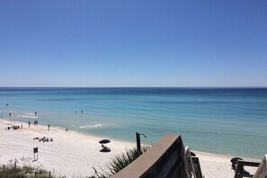 Ein Strand mit klarem, blauem Wasser, sandigem Ufer und einigen Personen.