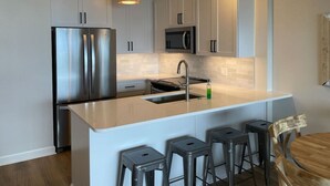 A modern kitchen with white cabinets, stainless steel appliances, a central island with bar stools, and recessed lighting.