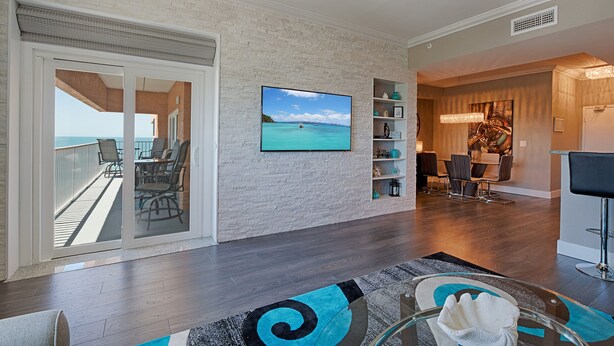 Una sala de estar moderna con un televisor grande, un comedor y un balcón con vistas al mar.