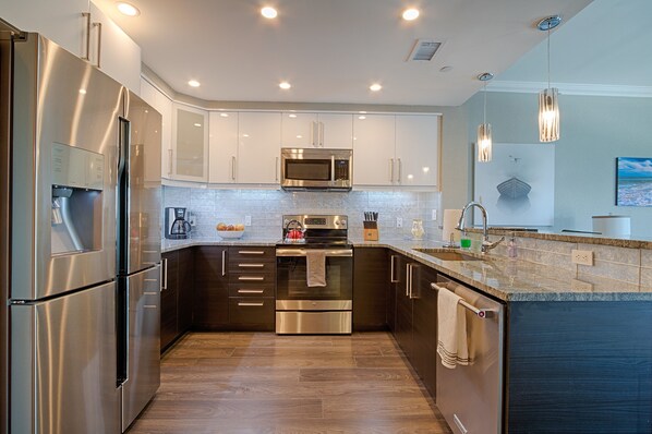 A modern kitchen with stainless steel appliances, white cabinets, and a granite countertop.