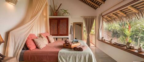 A bedroom with a bed, a ceiling fan, a window with a view of greenery, and a shelf with decorative items.