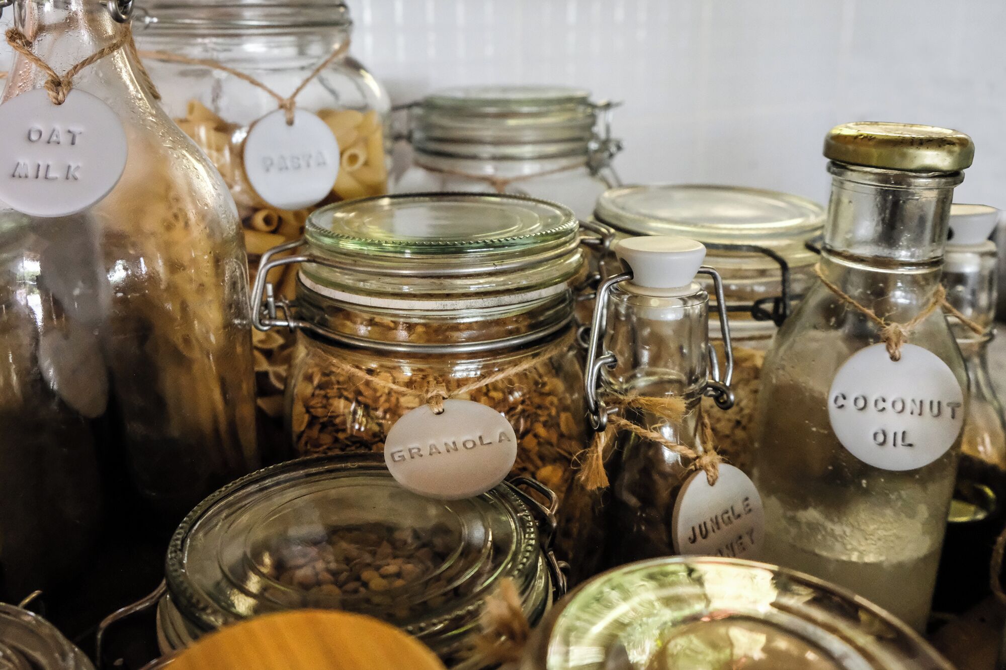 Différents pots en verre, tous étiquetés, certains contenant des céréales et d’autres des liquides, comme de l’huile de coco.