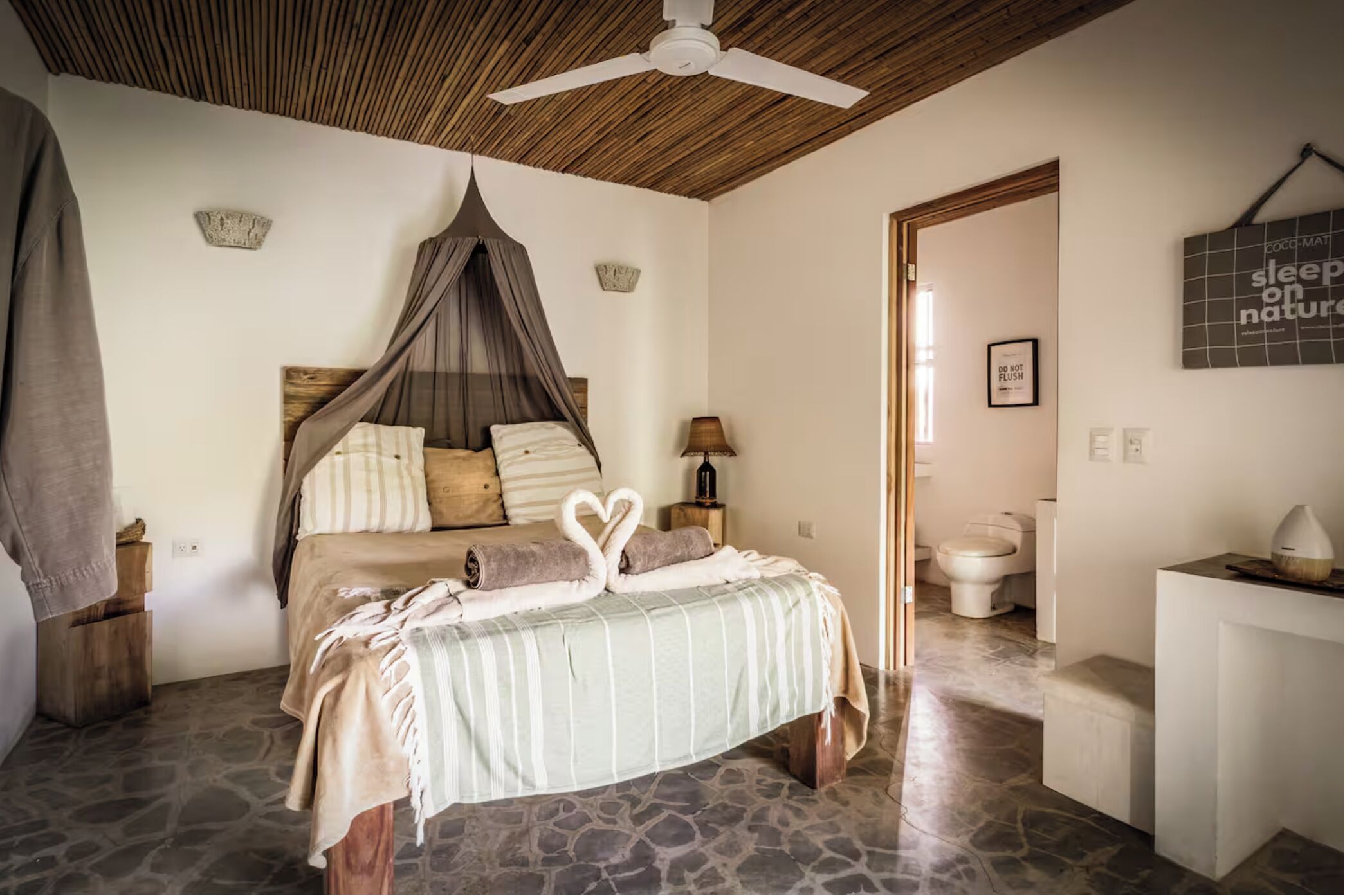 Une chambre à coucher avec un lit à baldaquin, une table de chevet, une commode, une horloge murale et une salle de bain avec des toilettes et un lavabo.