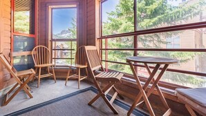 Una habitación acogedora con paredes de madera y ventanas amplias que ofrecen vistas a árboles y edificios. Hay dos sillas de madera y una mesa pequeña.