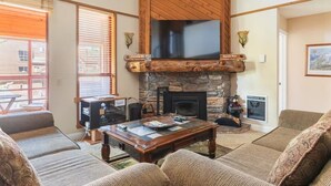 Una sala de estar acogedora con chimenea de piedra, vigas de madera y un televisor de pantalla plana grande.
