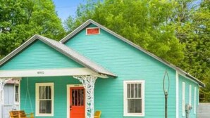 Una casa turquesa con un porche, una silla mecedora y una puerta roja.