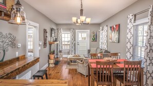 Un comedor con una mesa y sillas de madera, una araña y vista a la cocina.
