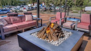 Zona exterior con asientos al aire libre, una chimenea, sillas acolchadas y vistas a un estacionamiento y colinas boscosas.