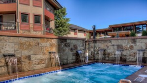Una piscina con múltiples fuentes, paredes de piedra y un edificio con balcones al fondo.