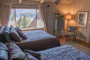 A bedroom with two beds, a view of a forest and lake, a lamp, and a chair. - Breathtaking Lake Views from every room! (Lake Arrowhead)