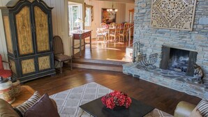 A living room with a fireplace, wooden furniture, and a dining area in the background.
