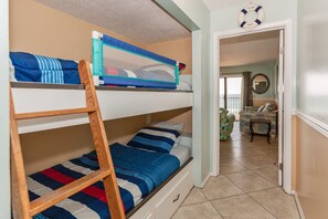 Une chambre avec un lit superposé, une échelle, une chaise et une porte donnant sur une autre pièce.