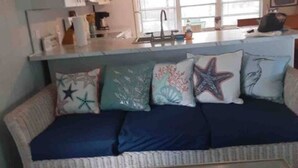 Een woonkamer met een bank, een bijzettafeltje met schelpen, en een keuken op de achtergrond.