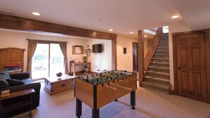 Ett mysigt vardagsrum med ett fotbollsspel, en soffa, ett skrivbord och en trappa som leder upp till ett annat plan.