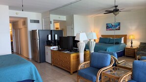 Habitación de hotel con cama, escritorio con computadora, televisor, refrigerador y área de comedor con mesa y sillas.