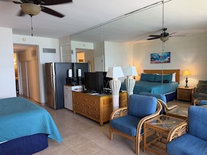 A hotel room with a bed, a desk with a computer, a television, a refrigerator, and a dining area with a table and chairs.