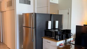 Una kitchenette compacta con refrigerador de acero inoxidable, microondas, cafetera y televisor.