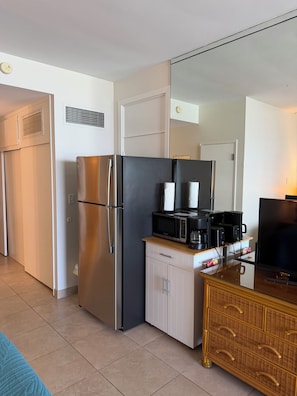 A compact kitchenette with a stainless steel refrigerator, a microwave, a coffee maker, and a television.