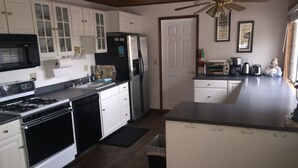 A kitchen with white cabinets, a black stove, a refrigerator, and a ceiling fan. - 2bd2bth CABIN with  WIFI,  HotTub,  Full Kitchen, smart tv/ Book1week get 20%off (Big Bear Lake)