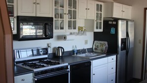 A compact kitchen with white cabinets, a black microwave, a stainless steel refrigerator, and a dishwasher. - 2bd2bth CABIN with  WIFI,  HotTub,  Full Kitchen, smart tv/ Book1week get 20%off (Big Bear Lake)