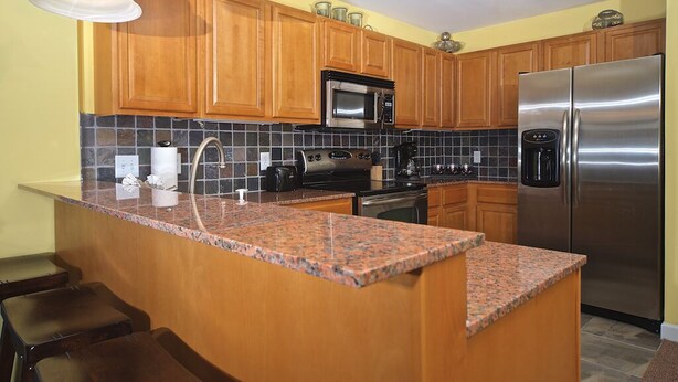A kitchen with wooden cabinets, granite countertops, stainless steel appliances, and a bar area with stools.