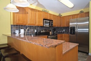 A kitchen with wooden cabinets, granite countertops, stainless steel appliances, and a bar area with stools. - Luxury Spacious Riverfront Condo in Perfect Location near Tanger Outlets (Sevierville)