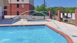 A swimming pool with a curved glass enclosure, surrounded by a brick building and a metal fence.