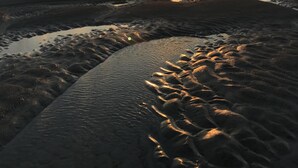 Escena de playa con el sol poniéndose en el horizonte, proyectando un brillo cálido sobre la arena y el agua.