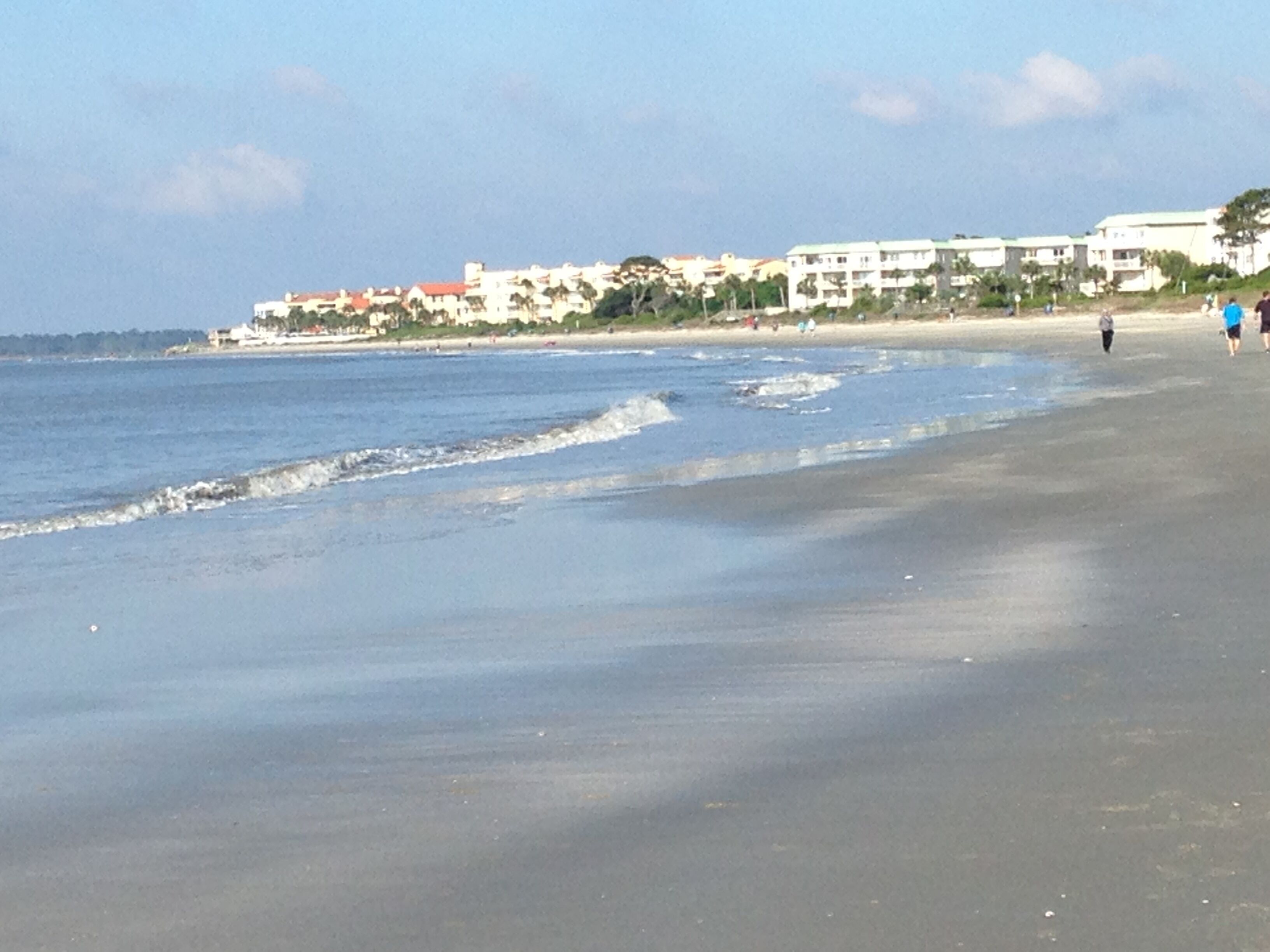 A beach with a sandy shore and a few buildings in the background.