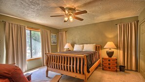 A bedroom with a wooden bed, two bedside lamps, a ceiling fan, and a window with curtains. - This quaint cottage is the perfect home base for your Yosemite trip. (Mariposa)