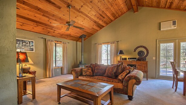 A cozy living room with a wooden ceiling, a sofa, a coffee table, and a fireplace. - This quaint cottage is the perfect home base for your Yosemite trip. (Mariposa)