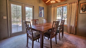 A dining area with a wooden table and chairs, large windows, and a ceiling fan. - This quaint cottage is the perfect home base for your Yosemite trip. (Mariposa)