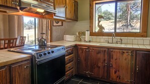 A kitchen with wooden cabinets, a stove, and a window overlooking a natural landscape. - This quaint cottage is the perfect home base for your Yosemite trip. (Mariposa)