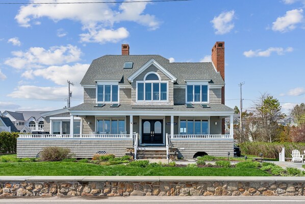 A two-story house with a front porch, a chimney, and a stone wall in front. - Spectacular Oceanfront Beach House on Gooch's Beach (Kennebunk)