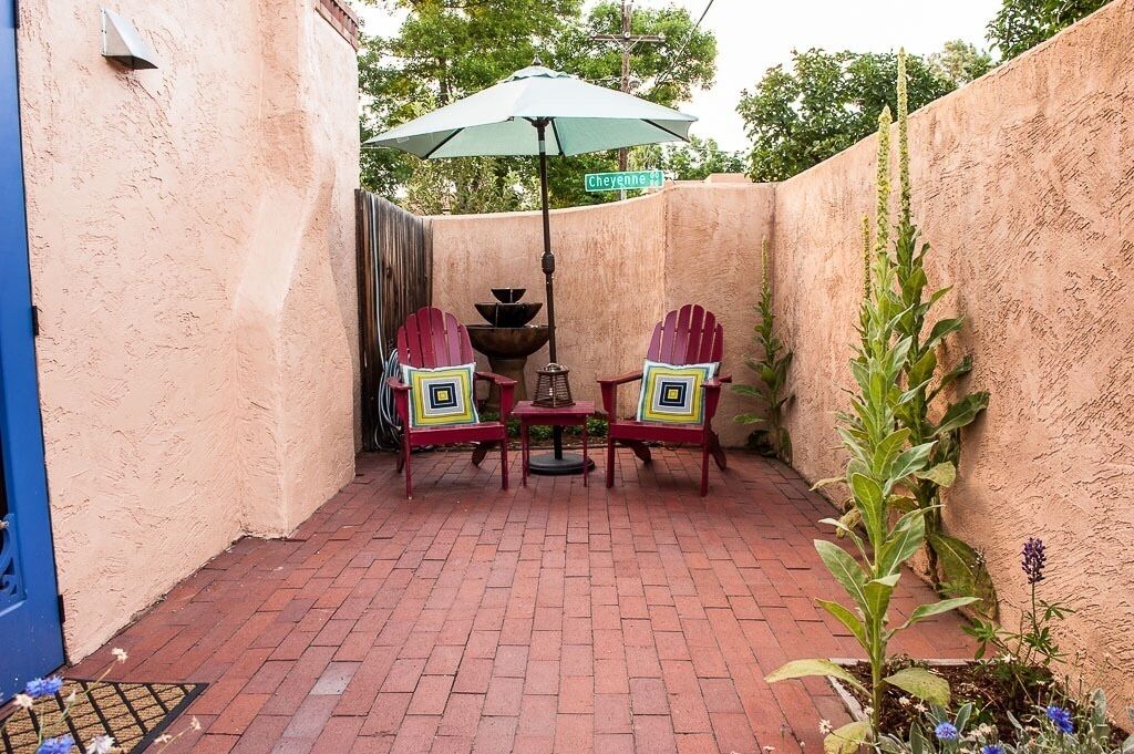 A patio with two Adirondack chairs, a table, and a green umbrella.