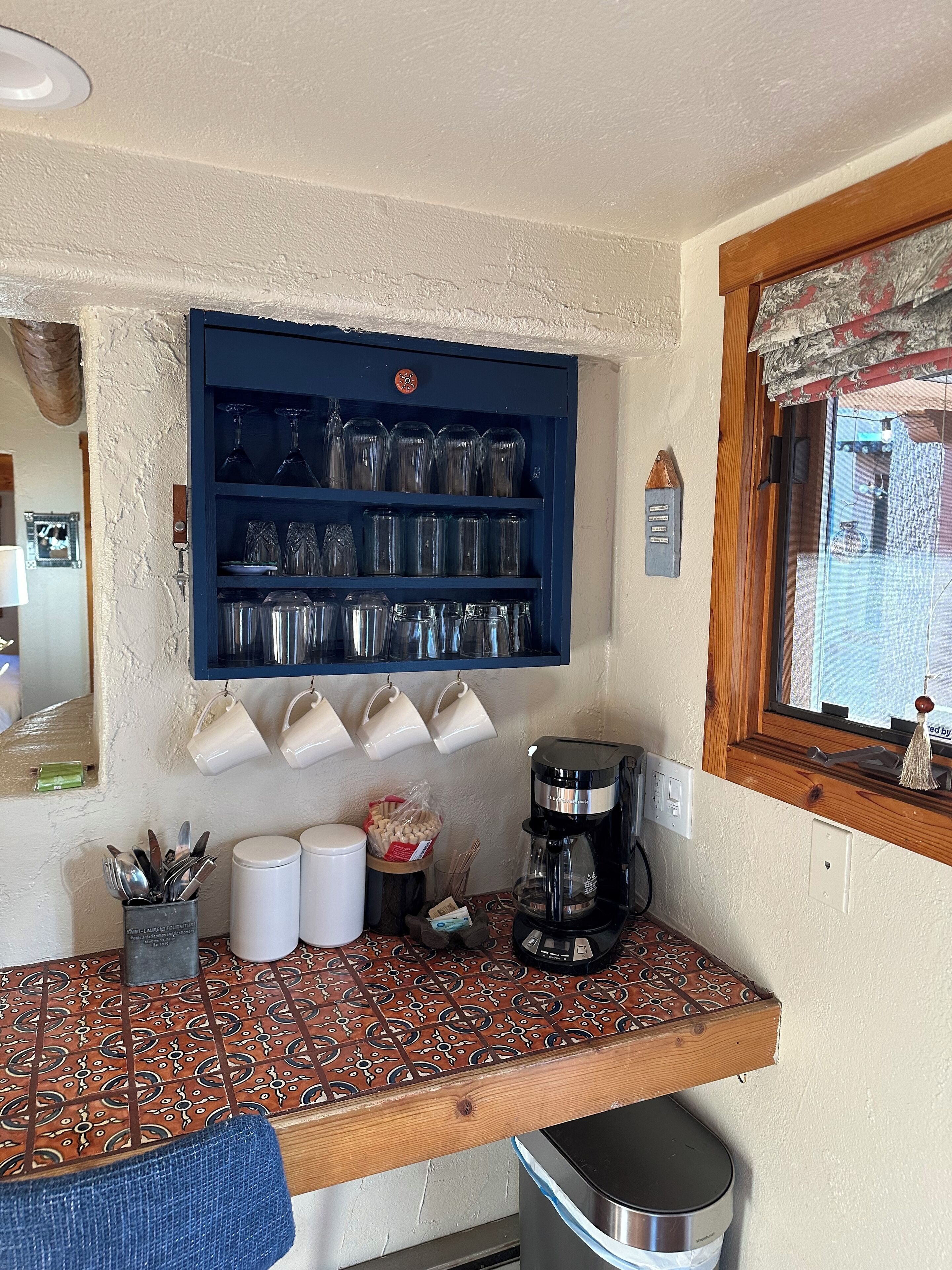 A kitchen with a blue shelf holding glassware, a coffee maker, and a patterned countertop.